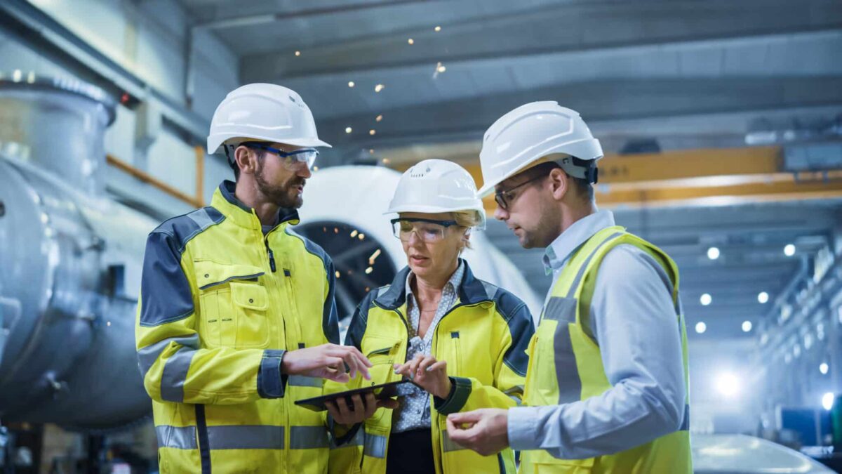 Three Heavy Industry Engineers Stand in Pipe Manufacturing Factory